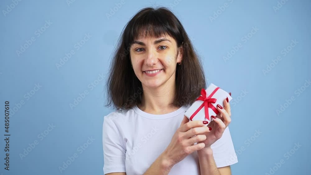 Beautiful smiling woman holding gift box in hand on blue wall background. Girl is happy with present Beautiful smiling woman holding gift box in hand on blue wall background. Girl is happy with present