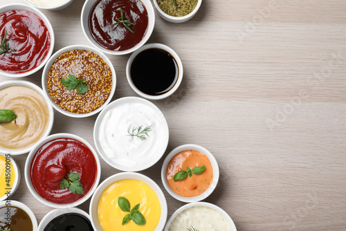 Many different sauces and herbs on wooden table, flat lay. Space for text