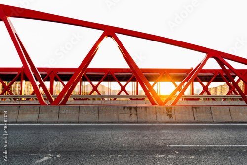 Road and red bridge at sunset, with the sun between the structure. Alicante red bridge