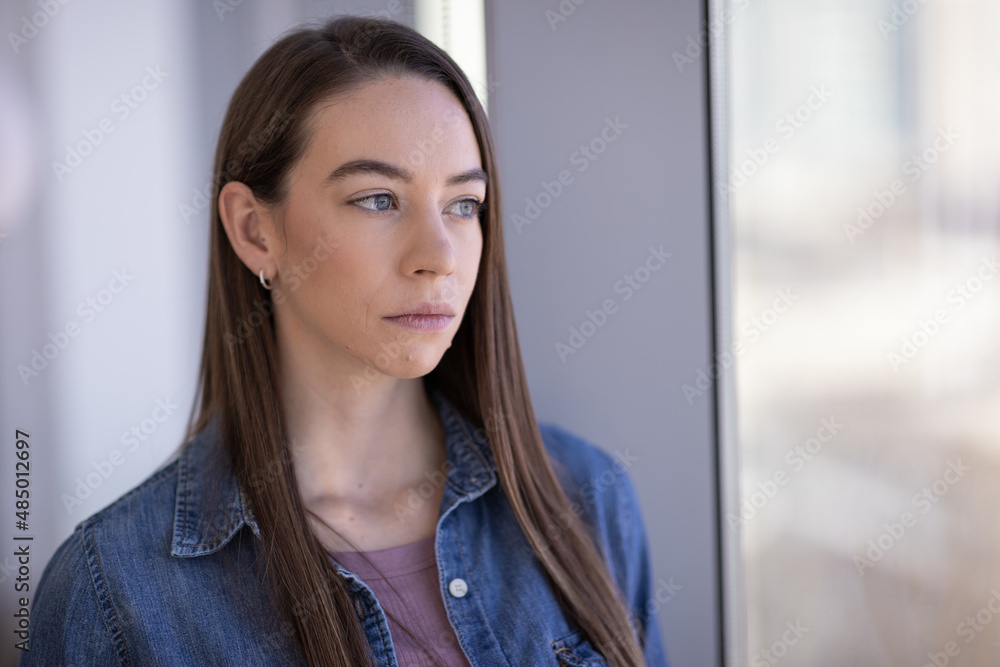 Caucasian woman sad serious face portrait standing by a window