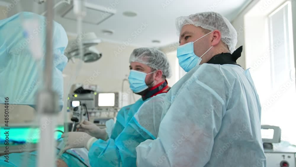 Surgeon applied surgical tools to a patient and another doctor helps him consulting. Specialists look at the screen and agree on something nodding heads. Surgeon applied surgical tools to a patient and another doctor helps him consulting. Specialists look at the screen and agree on something nodding heads.