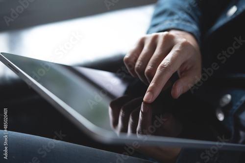 Close up of woman hand holding digital tablet pc and finger touching or pointing on touch screen with reflection, business and technology concept