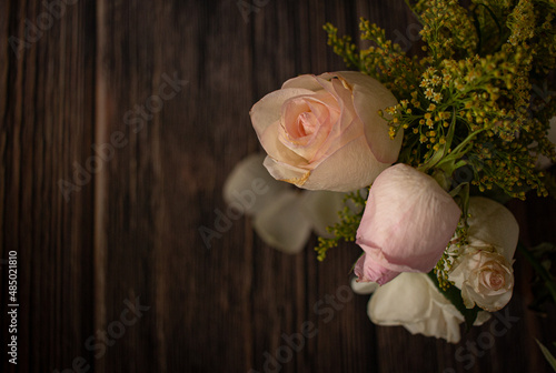beautiful romantic nostalgic background with bouquet of pastel color roses and small yellow flowers on dark wood floor © Evgenia