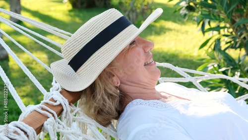 Beautiful senior woman smiling happy relaxing on a hammock enjoying the fresh air on the palm terrace. Senior citizen lifestyle concept