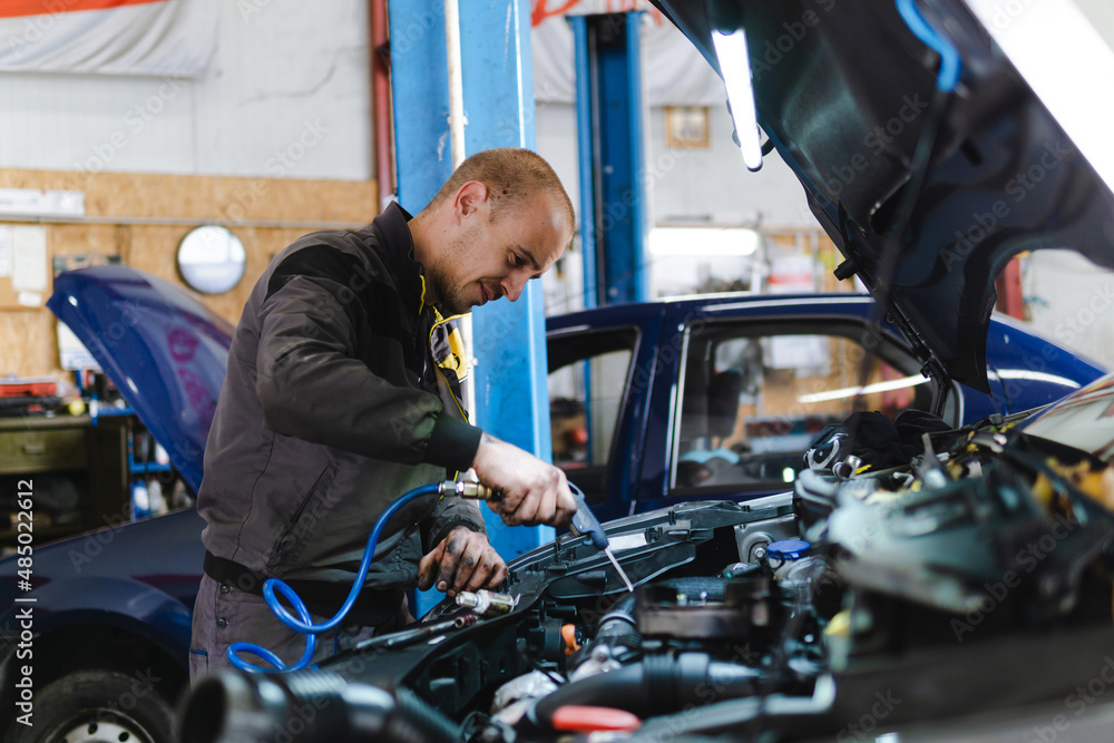 Handsome mechanic in uniform is working in auto service garage. Repair service. Handsome mechanic in uniform is working in auto service garage. Repair service.
