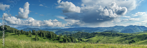 Picturesque valley, panoramic mountain view. Bright sunlight, spring greens of forests and meadows.