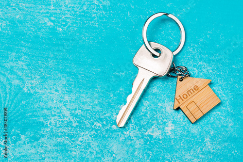 Wooden house shaped keychain and key on blue wooden background. Free space © Nikolay N. Antonov