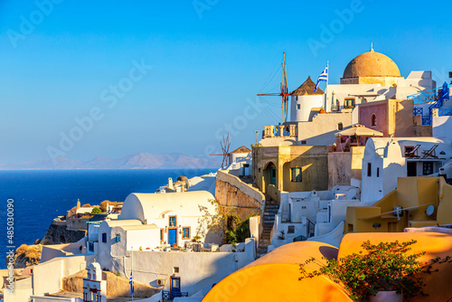 Famous Oia village with traditional white houses and windmills during summer sunny day Santorini island, Greece. Greece vacation iconic background.