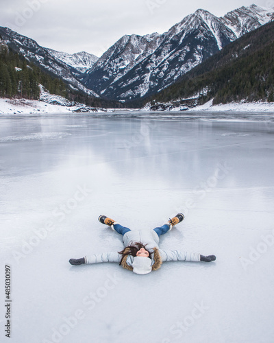 Woman laying on a frozen lake in Montana during the winter in mountains