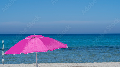 Isolated fuchsia or pink beach umbrella. Blue sky. Relaxing context. Summer holidays at the sea. General contest and location. Turquoise sea and white beach in the background