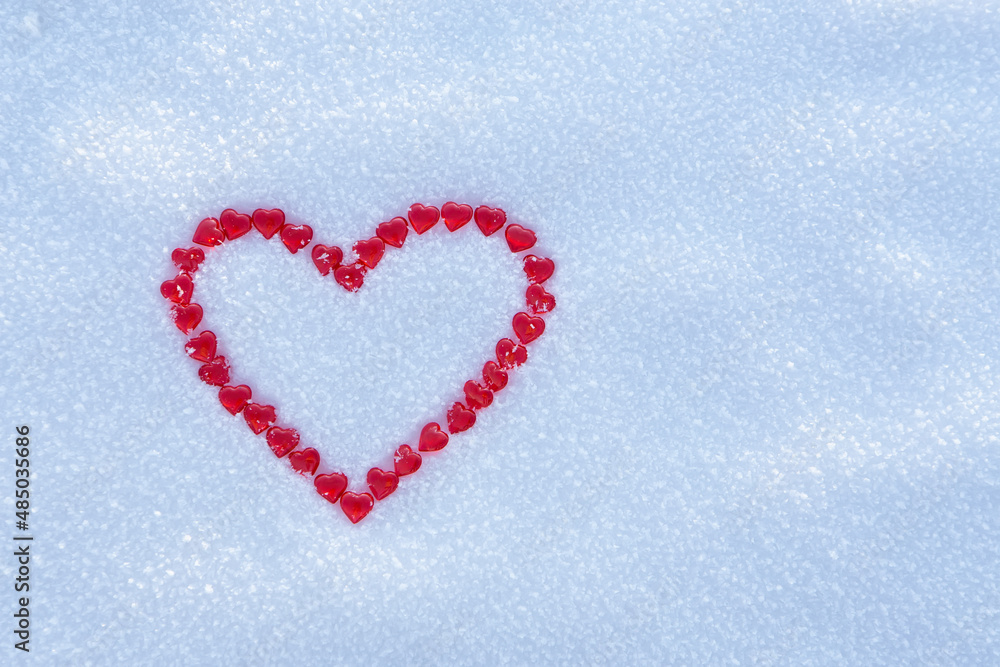Red heart made with lots of little hearts on snow surface.