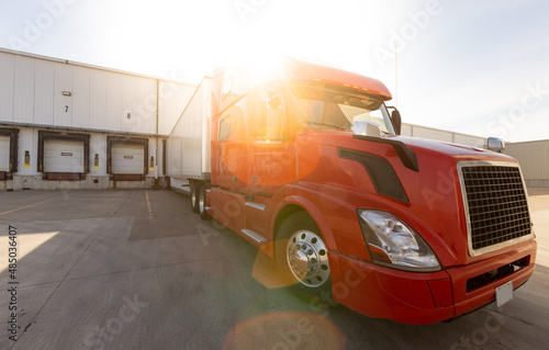 Wide angle of American Semi Truck parked at the dock. Tucking and logistics with red big rig waiting to get loaded at company. Shipping and receiving in the transportation business on a sunny day. photo