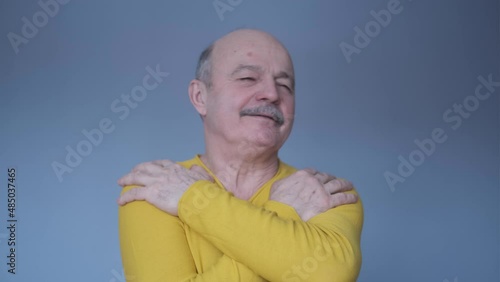 Confident smiling man holding hugging himself isolated on blue wall background