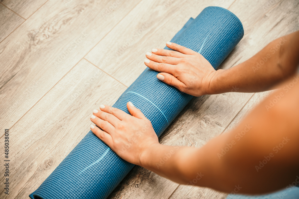 Woman hands rolled up yoga mat on gym floor in yoga fitness training