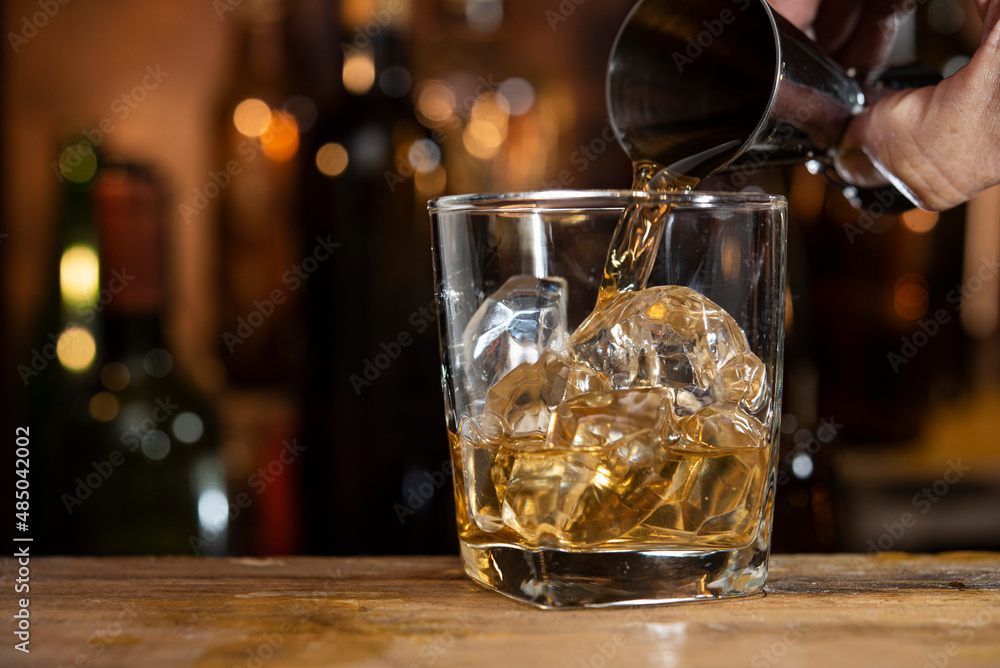 whisky pouring from jigger into glass of ice whisky pouring from jigger into glass of ice