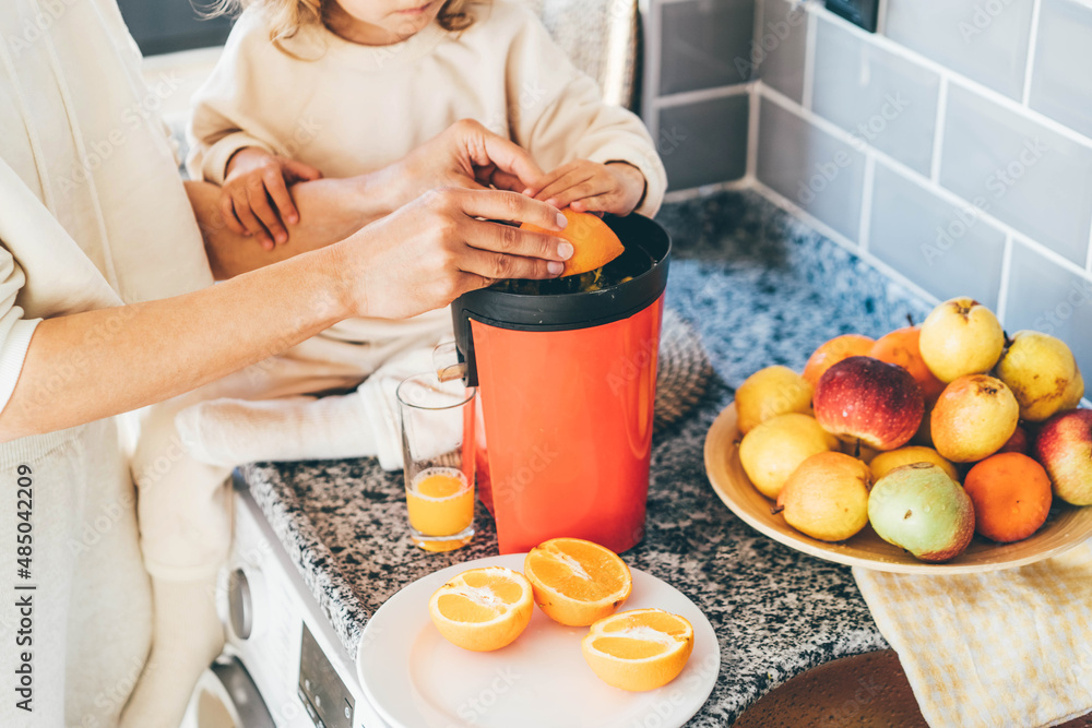 Little baby girl with mother makes freshly orange juice. Stock Photo