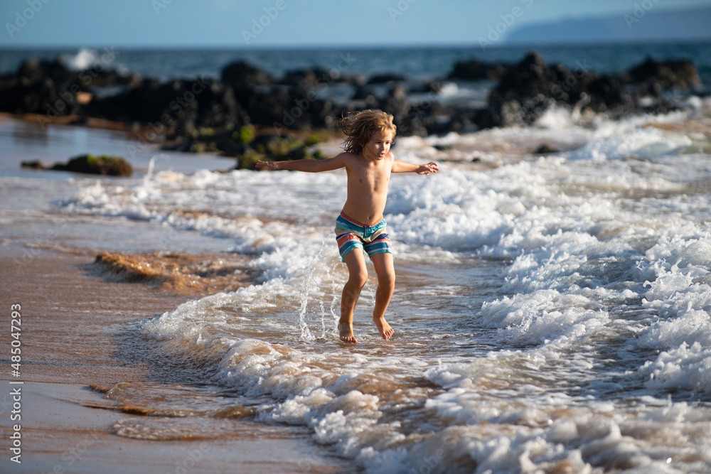 Child playing on ocean beach. Kid jumping in the waves at sea vacation. Little boy running on tropical beach of exotic island during summer holiday.