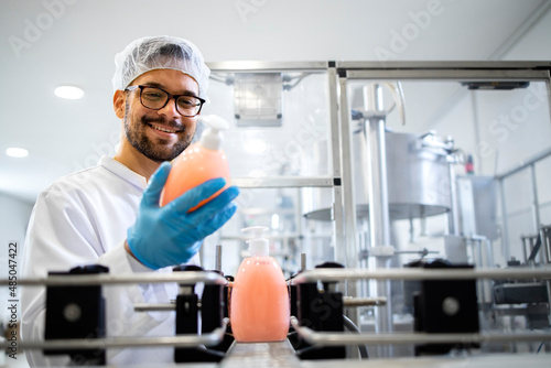 Production line worker or technologist in white sterile uniform working in chemical industry and checking quality of liquid soap or detergent in factory.