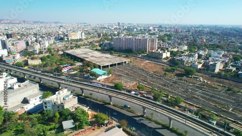 aerial drone shot going towards busy street, elevated metro train tracks, railway yard and skyscraper in the distance showing the space given to public transport in the busy cities of India photo