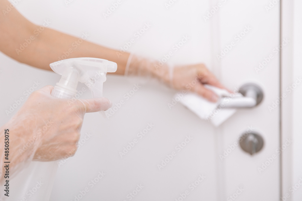 Cleaning door handles with wet wipe and white gloves. Woman hand using towel for cleaning home room door link. Sanitize surfaces prevention in hospital and public spaces against corona virus Cleaning door handles with wet wipe and white gloves. Woman hand using towel for cleaning home room door link. Sanitize surfaces prevention in hospital and public spaces against corona virus