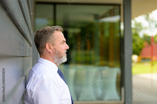 Side view portrait of a senior man standing waiting in town