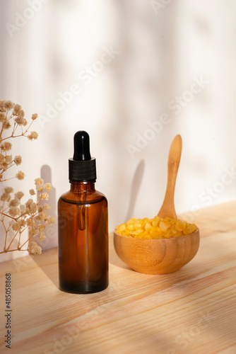 Dropper bottle with essential oil. Wooden bowl with yellow bath sea salt. Beauty treatment for spa and wellness on natural wooden background . Skincare natural cosmetic concept for body care
