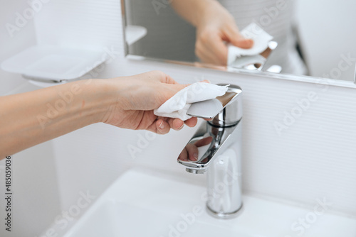 Cleaning the sink faucet with a microfiber cloth. Cleaning the bathroom. Sanitize surfaces prevention in hospital and public spaces against corona virus. Woman hand using wet wipe