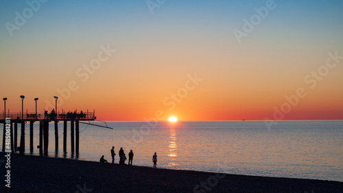 Colorful seascape, sunset shot and red sky. Beach and pier with people silhouette in backlight, coastal sunlight on water