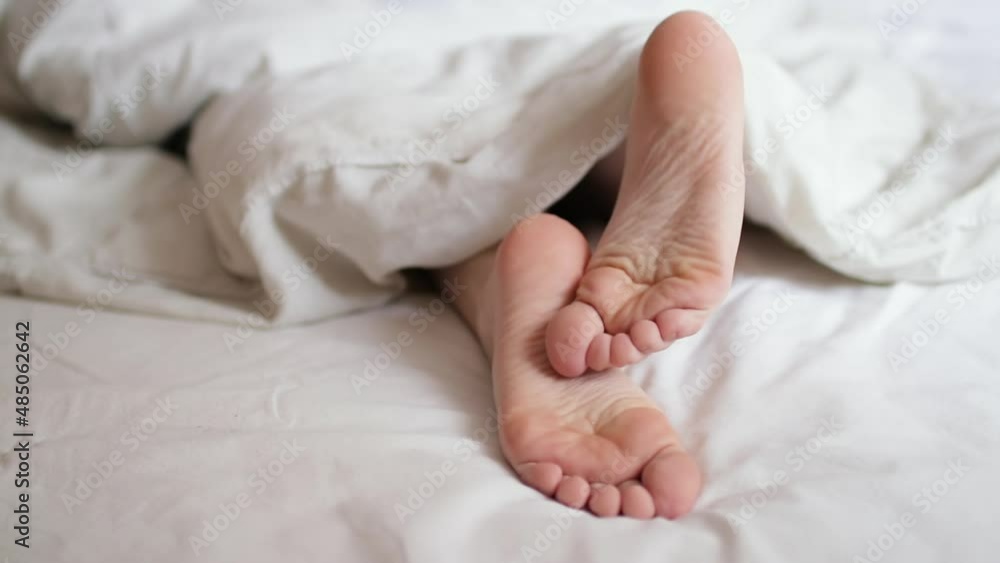 Woman legs under the covers in bed, close up. Morning and waking up. Woman legs under the covers in bed, close up. Morning and waking up.