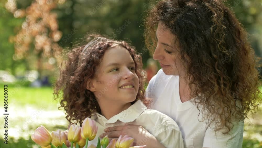 Portrait of a woman with a bouquet of tulips hugging her teenage daughter. Mothers Day. Portrait of a woman with a bouquet of tulips hugging her teenage daughter. Mothers Day.