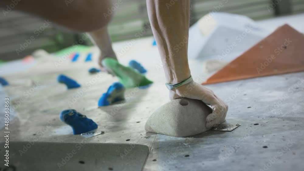 Bottom view: A sporty Caucasian man climbs a bouldering wall. Moves legs on ledges. Practices climbing on an artificial indoor wall. Extreme sports, active lifestyle. Training on the climbing wall. Bottom view: A sporty Caucasian man climbs a bouldering wall. Moves legs on ledges. Practices climbing on an artificial indoor wall. Extreme sports, active lifestyle. Training on the climbing wall.