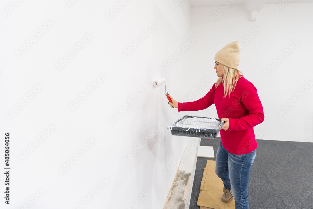 Close up. Side view of pretty joyful Caucasian woman alone painting room in new house. Beautiful female renovating home painting wall using roller brush redesigning apartment Close up. Side view of pretty joyful Caucasian woman alone painting room in new house. Beautiful female renovating home painting wall using roller brush redesigning apartment