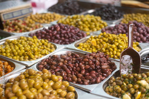 Different colors and taste olives in plastic boxes on stall in foreground. Market. Traditional arabic and jewish food. Vegetarian. Healthy food, lifestyle. Close-up