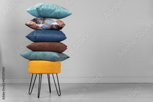 Yellow pouf on steel legs with pillows in a stack, on a gray background. Space for text