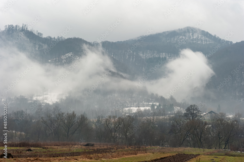 White fog on the background of forest mountains draws the news of the approach of spring.