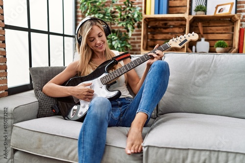 Young blonde woman smiling confident playing electric guitar at home