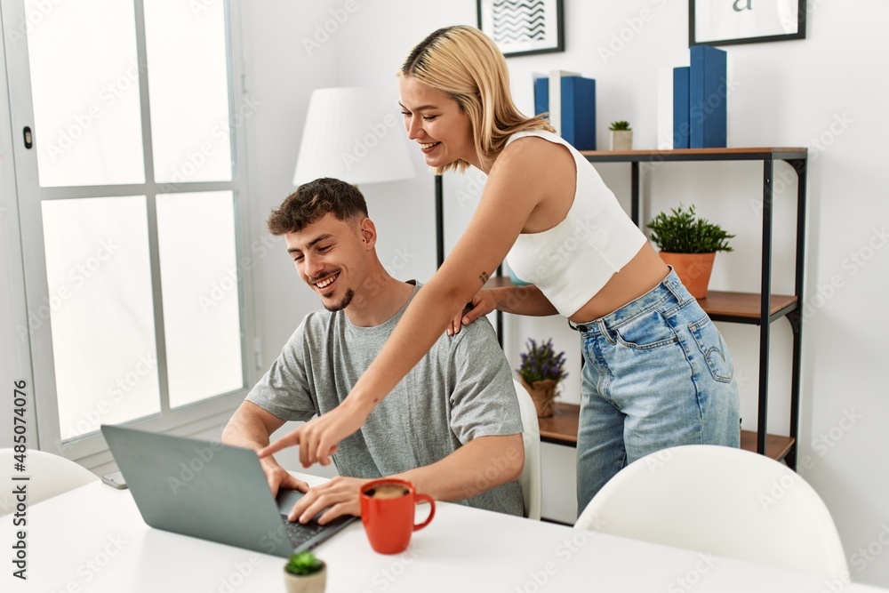 Obraz premium Young caucasian couple using laptop and drinking coffee sitting on the table at home.
