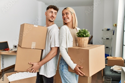Young caucasian couple smiling happy holding cardboard boxes standing at new home. © Krakenimages.com
