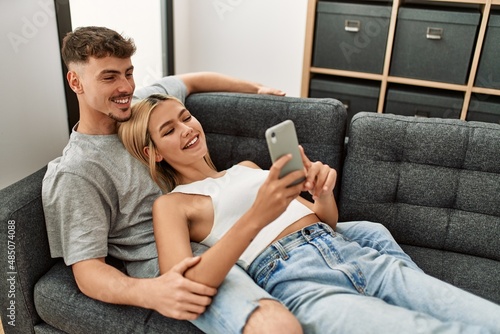 Young caucasian couple smiling happy using smartphone at home.