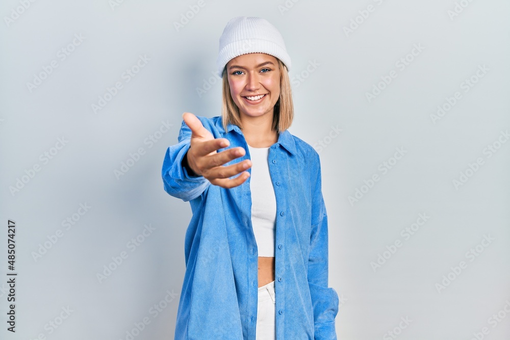 Beautiful blonde woman wearing wool hat smiling cheerful offering palm hand giving assistance and acceptance. Beautiful blonde woman wearing wool hat smiling cheerful offering palm hand giving assistance and acceptance.