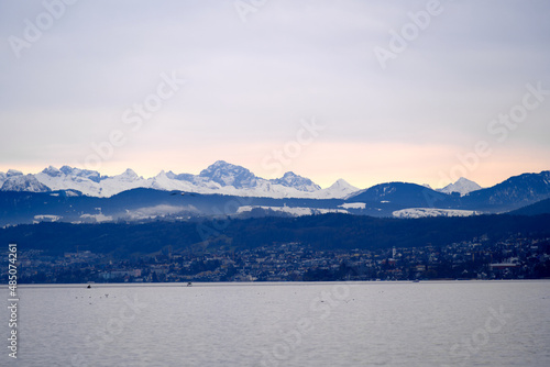 Beautiful scenic landscape with Lake Zurich in the foreground and Swiss Alps in the background on a cloudy winter afternoon. Photo taken February 3rd, 2022, Zurich, Switzerland.