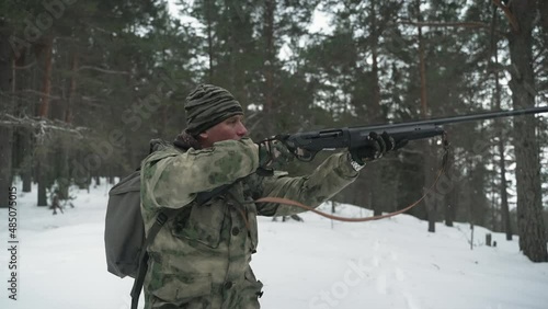 Wallpaper Mural A hunter in camouflage clothing walks through the winter forest . A man removes a gun from his shoulder, preparing to shoot Torontodigital.ca