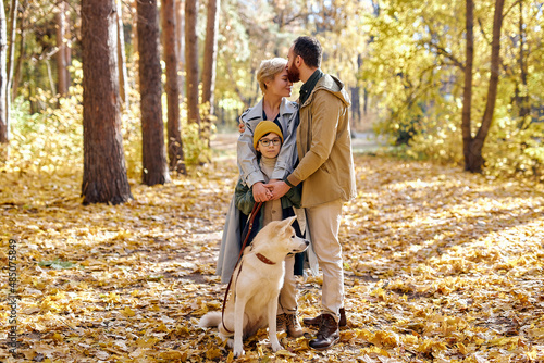Portrait Of happy family with pet dog akita inu walking in autumn park or forest, bright colorful yellow leaves around. young man, woman and kid lead active lifestyle. human emotions concept © Roman
