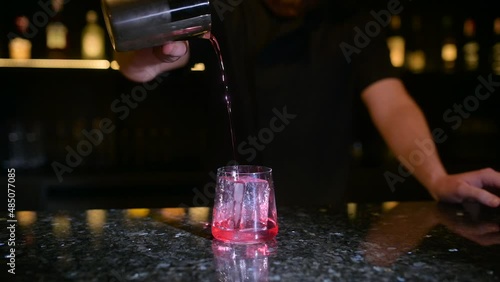 Professional bartender creating a cocktail drink. Bartender is preparing an alcoholic cocktail with ice cubes to customers at the bar. Night life