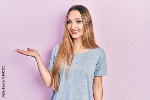 Young blonde girl wearing casual t shirt smiling cheerful presenting and pointing with palm of hand looking at the camera.