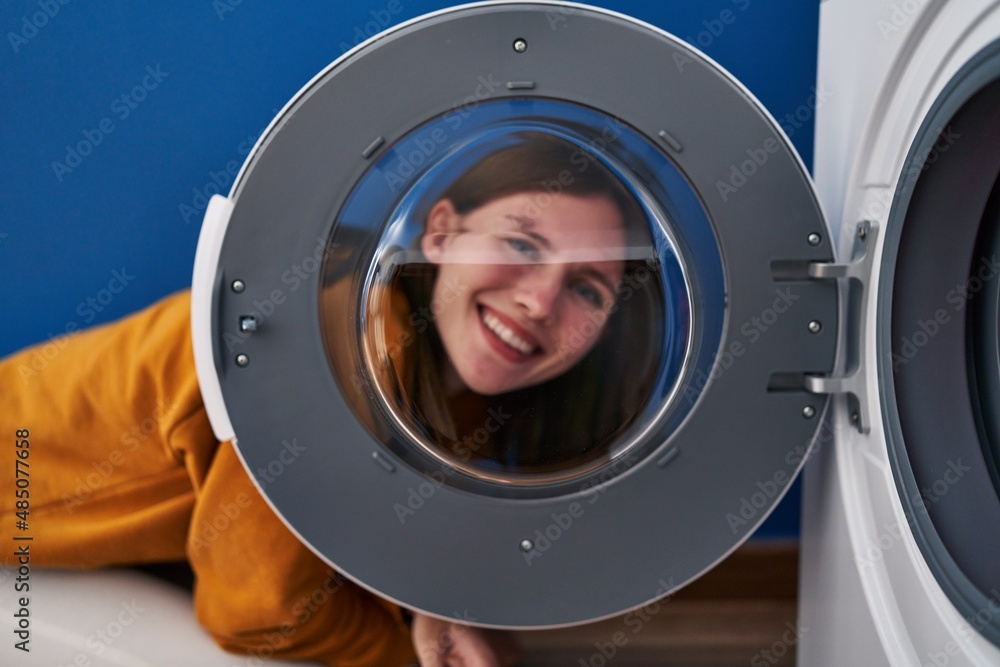 Young brunette woman looking through the washing machine window smiling with a happy and cool smile on face. showing teeth.