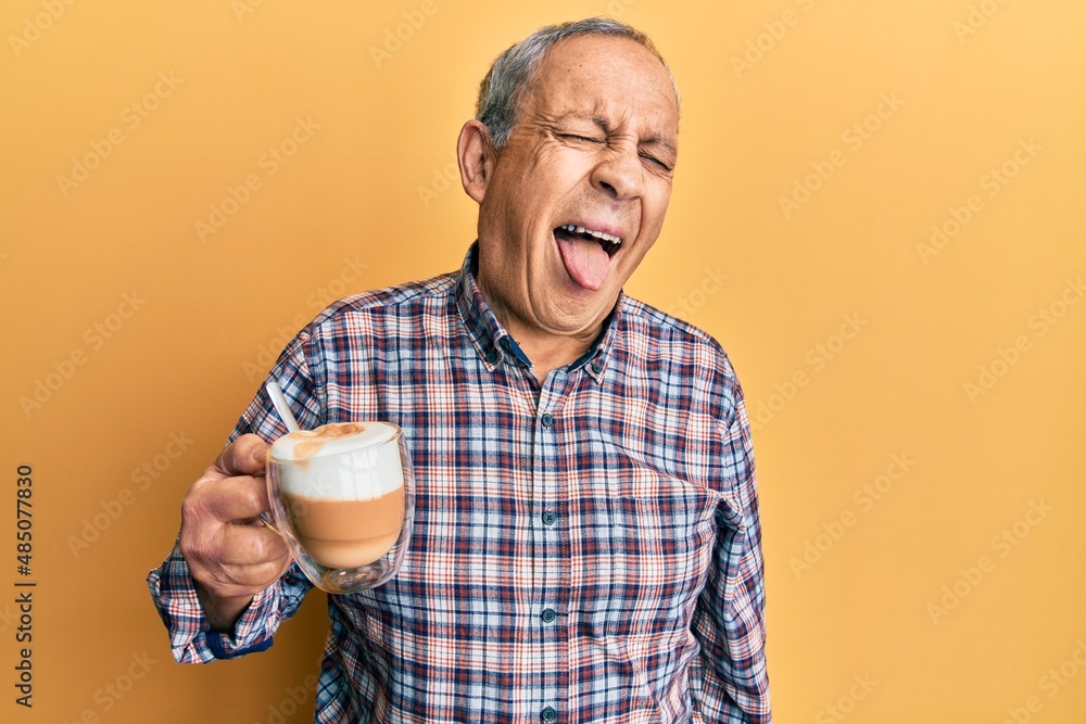 Handsome senior man with grey hair drinking a cup coffee sticking tongue out happy with funny expression. emotion concept. Handsome senior man with grey hair drinking a cup coffee sticking tongue out happy with funny expression. emotion concept.