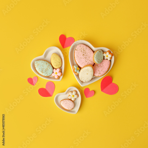 Sweets, pastry, gingerbread cookies for Easter table. Easter eggs heart shaped decor on yellow background top view copy space, spring seasonal holiday banner for your site, flyer, coupon