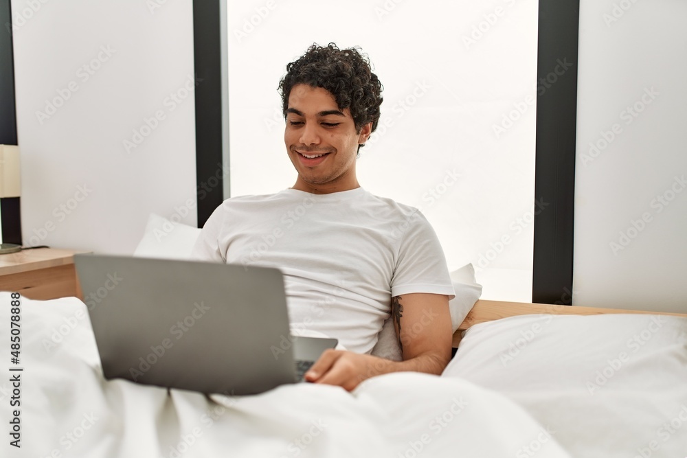 Young hispanic man using laptop sitting on the bed at bedroom. Young hispanic man using laptop sitting on the bed at bedroom.