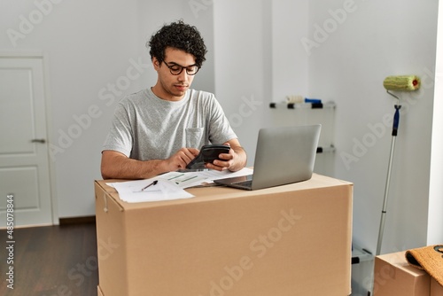 Young hispanic man calculate economy using laptop at new home.
